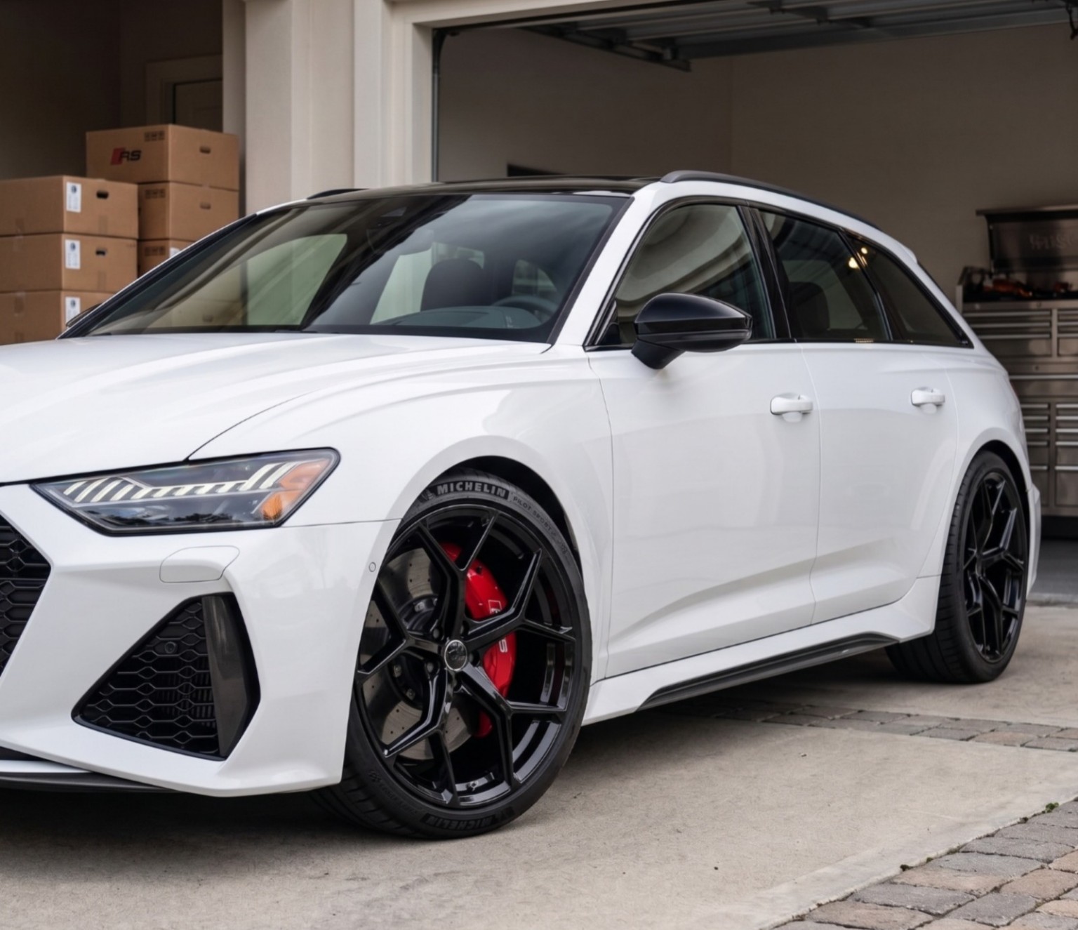 White Audi RS6 Avant fitted with 20-inch gloss black RS6 style alloy wheels and performance tyres parked outside a premium garage.