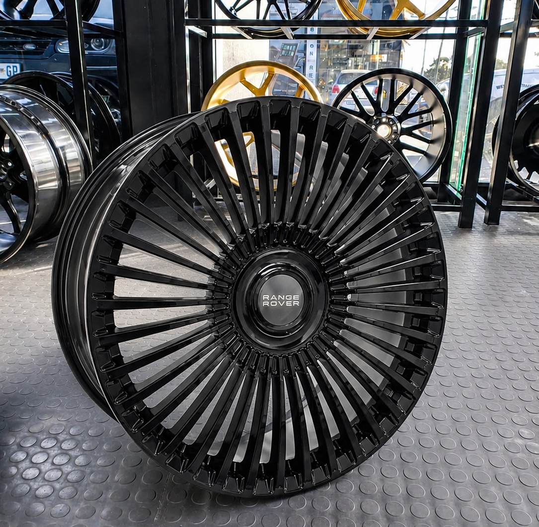 Single 22-inch gloss black multi-spoke Range Rover alloy wheel on display in an automotive shop showroom.